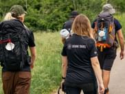 Grupp vandrare med ryggsäckar på asfalterad stig genom grön landsbygd. Kvinna bär Bering Travel-tröja på Portugisiska Caminon.