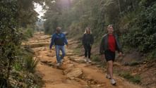 Tre vandrare går nerför en sandig stig omgiven av tät grön vegetation på Sri Lanka, på väg mot World's End.