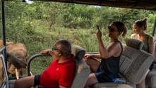 Tre turister i ett öppet safarifordon fotograferar elefanter i Sri Lanka. En guide i röd skjorta kör medan passagerarna tar foton.