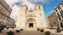 Romanesque cathedral with twin towers and ornate entrance on town square in Portugal, surrounded by traditional buildings and planters.