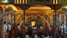 Interiör av utsmyckat buddhistiskt tempel i Kandy med gyllene dekorationer, snidade pelare och besökare samlade kring centrala helgedom.