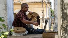 Ormtjusare i randig skjorta spelar flöjt för en kobra som kommer ur en korg i Galle, Sri Lanka, med koloniala byggnader i bakgrunden.