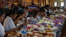 Stor gruppe mennesker i hvidt tøj deltager i en buddhistisk ceremoni i Kandy, med farverige blomsterofre spredt på borde.