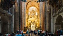 Indre af Santiago de Compostela-katedralen der viser ornamenteret gyldent barok-alterbillede med besøgende i skibet under stenbuer.
