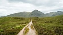 Grusvej på West Highland Way gennem grøn hede mod bjerge under overskyet himmel i Skotland.