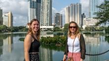 Två leende kvinnor vid Beira Lake i Colombo med moderna höghus reflekterade i det lugna vattnet.