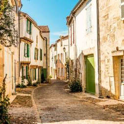 Smal brostensgade i La Rochelle med traditionelle franske stenhuse, grønne skodder og blomstrende slyngplanter.