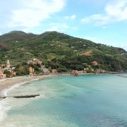 Aerial view of a Cinque Terre coastal village with colorful houses along a curved beach, surrounded by green hills and turquoise sea.