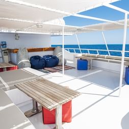 Øverste dæk på MV Tala med hvide siddeområder, træbord med røde bænke og panoramaudsigt over havet under delvis overdækning.