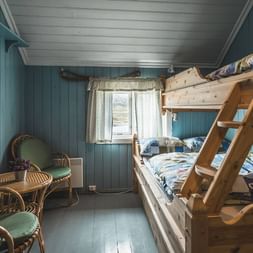 Hyggeligt soveværelse i Geiterygghytta DNT-hytte med træstokke senge, blå panelvægge, hvidt loft og kurvstole ved vinduet.