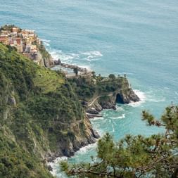 Aerial view of colorful houses in Cinque Terre village perched on dramatic cliffs above turquoise Mediterranean Sea with lush green vegetation.