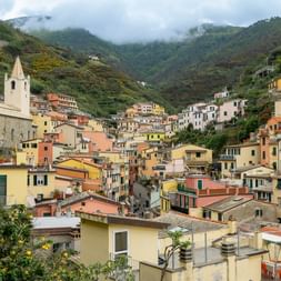 Colorful houses of a Cinque Terre village cascading down a steep hillside with a white church bell tower prominently featured among the buildings.