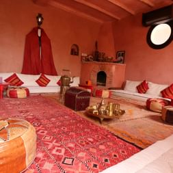 Traditionel marokkansk salon Atlas Kasbah Traditionel marokkansk salon med hvide polstrede siddepladser, rødstribede puder, læderpuder, udsmykkede tæpper og terrakottavægge.