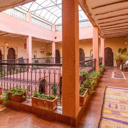 Atlas Kasbah Ecolodge indre patio Traditionel marokkansk riad-interiør på Atlas Kasbah Ecolodge med terrakottavægge, træbjælker, glastag og farverige tæpper.