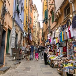 Narrow cobblestone street in Cinque Terre lined with colorful buildings and tourist shops selling souvenirs, postcards and clothing.