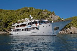 Vit motoryacht MY Mystic ankrad i lugna blå vatten längs den kroatiska kusten med skogklädda klippor i bakgrunden.