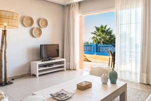 Lyst opholdsstue med hvide møbler, flettet dekoration og terrasseudsigt med palme på Paradis Plage resort i Marokko.