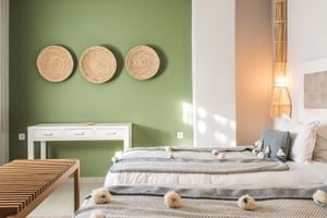 Rummelig Prestige Suite på Paradis Plage med grøn accentvæg, flettet kurvdekoration, hvidt konsolbord, to senge med kvastprydet tæpper og bambusbelysning.