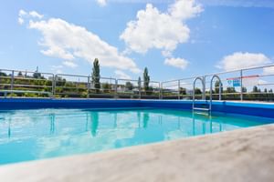 Simbassäng på MS SE-MANON med klart blått vatten, metallräcken och stege. Blå himmel med vita moln ovanför däcket.