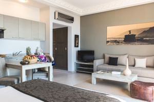 Moderne junior suite med åben stue, tekøkken, beige sofa, spisebord og kystkunstværk på væggen på Paradis Plage, Marokko.