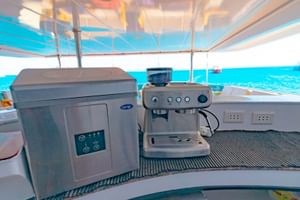 Kaffestation på Long Island liveaboard däck med espressomaskin och vattenautomat. Turkos hav synligt genom fönster.
