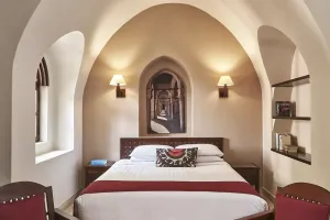 Hvælvet soveværelse med hvide vægge, dobbeltseng med hvidt sengetøj, mørkt træmøbler, væglamper og pyntepude på Sultan Bey El Gouna.