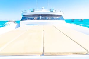 Rymligt soldäck på Long Island liveaboard med krämfärgade solstolar, vita räcken och turkost havsvatten under klar blå himmel.