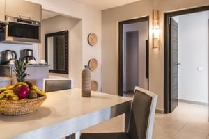 Moderne spiseplads i Prestige Suite på Paradis Plage, Marokko, med hvidt bord, stole, tekøkken og dekorative flet-elementer på beige vægge.