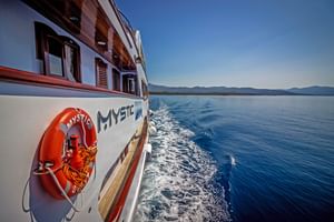 Sidovy av fartyget MY Mystic med orange livboj seglande genom blått Adriatiskt vatten. Kroatisk kustlinje med berg synlig i bakgrunden.
