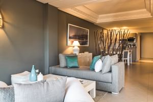 Moderne stue med grå sofa, turkise puder, hvidt sofabord og dekorativ grenskærm. Varm belysning og beige flisegulv.