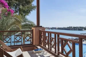 Balkon med liggestole og dekorativt trægelænder med udsigt over blå pool og lagune på Sultan Bey Hotel i El Gouna, Egypten.