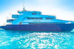 Long Island liveaboard-yacht med blått och mörkblått skrov förtöjd i turkost vatten under klar himmel.