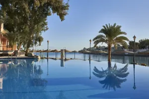 Infinity pool med palmereflektion på Sultan Bey El Gouna resort, med udsigt over lagune med bygninger og klar blå himmel.
