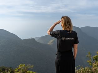 Kvinde i sort trøje skygger for øjnene mens hun ser på grønne bjergkæder i Sri Lanka under skyet himmel.