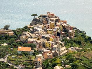 Flyfoto av en fargerik Cinque Terre landsby på et klippeframspring over Middelhavet med terrasserte vingårder.