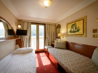 Skibskahyt med to enkeltsenge, træpaneler, TV, spejl, vindue med gardiner og vægkunst på MS Prinzessin Katharina.