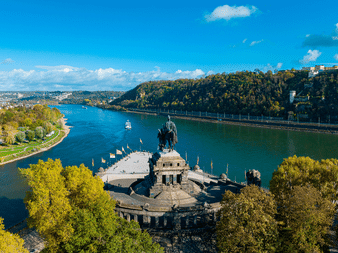 Luftfoto af Deutsches Eck monument i Koblenz, hvor Rhinen og Mosel mødes, med rytterstatue, grønne træer og fæstningsbakke.