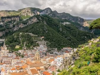 Farverig bjergby på Amalfikysten med terrakotta-tage indlejret mellem dramatiske kalkstensklipper og frodig grøn vegetation.