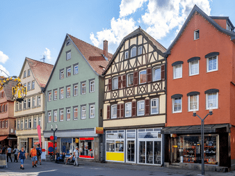 Række af traditionelle tyske bygninger i Bad Cannstatt med bindingsværkshus, grønne og orange facader og butikker i stueetagen.