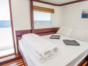 Ren skibskahyt på MV Tala med dobbeltseng, hvidt sengetøj, håndklæder og store vinduer der viser havudsigt og dæk udenfor.