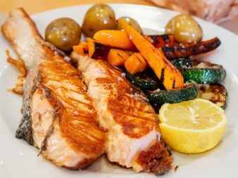 Grilled salmon fillet with lemon, roasted vegetables including carrots, zucchini, and potatoes on a white plate during Portuguese Camino day 8.