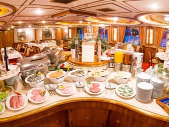 Elegant buffet på et Donau krydstogtskib med pålæg, salater og desserter. Udsmykket spisesal med dekoreret loft og vinduer.