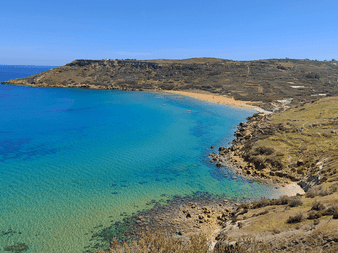 Luftfoto af Ramla Beach på Gozo med turkisblåt vand, gylden sandstrand og klippefyldte skråninger under klar himmel.