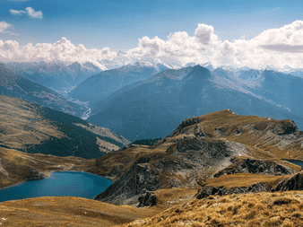 Blå bjergsø Lacs de Malrif i gyldne dale med klippefyldte toppe og snedækkede bjerge i Queyras under skyet himmel.