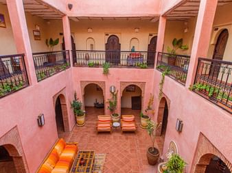 Atlas Kasbah gårdsplads patio i Marokko Traditionel marokkansk riad-gårdsplads med lyserøde vægge, to-etagers arkitektur, udsmykkede balkoner, orange siddeområde og potteplanter.