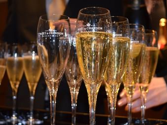 Multiple champagne flutes filled with golden Moët & Chandon champagne arranged on a tray, with a server's hand visible in the background.