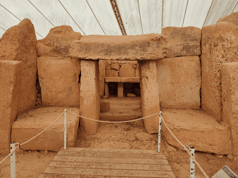 Interiør af det forhistoriske Hagar Qim tempel på Malta med massive kalkstensblokke og indgang under beskyttende teltoverdækning.