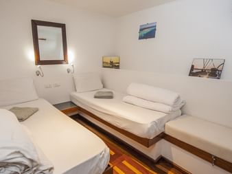 Ren hvid skibskahyt på MV Tala med to enkeltsenge, hvidt sengetøj, trægulve, spejl, maritime kunstværker og koøjer med naturligt lys.