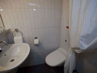 Kompakt badeværelse på MS Princess med hvid håndvask, toilet, flisebelagte vægge og hvidt brusegardiner.
