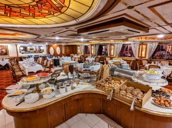 Elegant restaurant ombord på MS Prinzessin Katharina med buet buffetdisk, hvide duge og udsmykket loft.